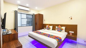 A hotel room with a bed, a desk, an air conditioning unit, a window with curtains, and a nightstand with a lamp. - Fabhotel Celebrity Inn (New Delhi)