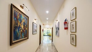 A hallway with framed artwork on the walls, a fire extinguisher, and a door at the end. - Fabhotel Celebrity Inn (New Delhi)