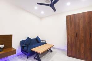 A room with a ceiling fan, a wooden wardrobe, a blue sofa with cushions, and a wooden table. - Fabhotel Celebrity Inn (New Delhi)