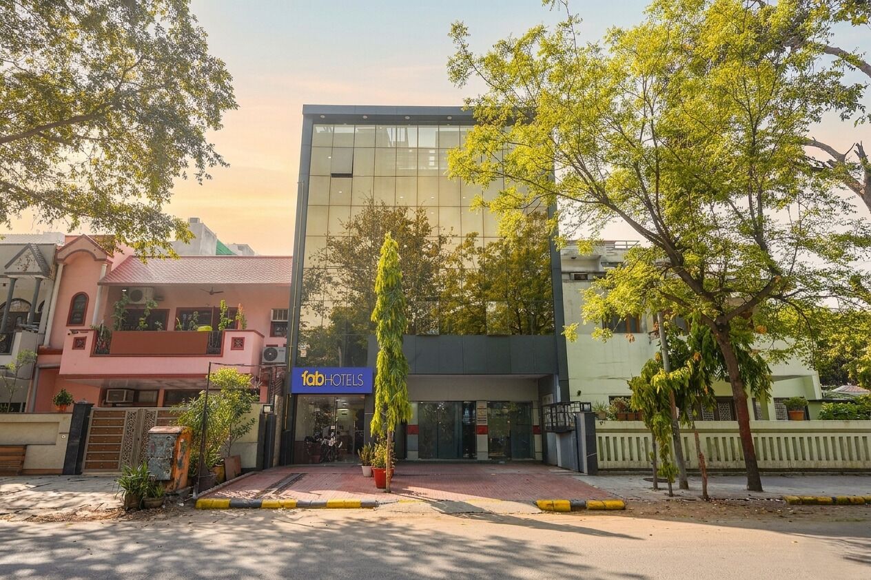 A modern building with a 'fabHOTELS' sign, surrounded by trees and other buildings.