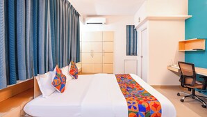A hotel room with a bed, a desk, a chair, a wardrobe, and a ceiling fan. - Fabhotel Krishna Sai (Pune)
