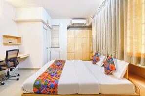 A hotel room with a bed, a desk, a chair, a wardrobe, and an air conditioning unit. - Fabhotel Krishna Sai (Pune)