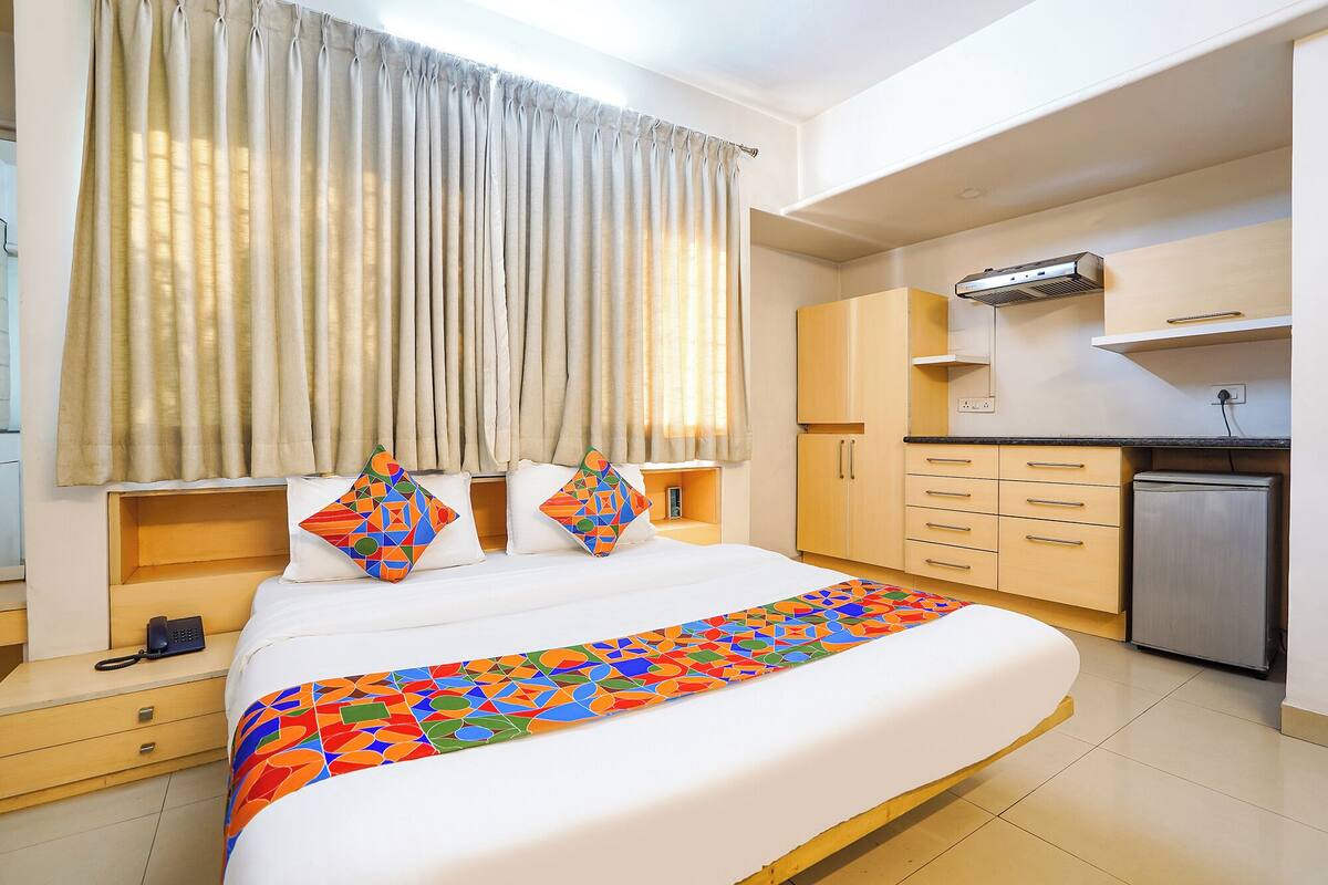 A hotel room with a bed, a desk, a phone, and a kitchenette.