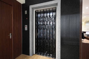 A modern elevator with a black metal gate, a wooden door, and a textured wall. - Fabhotel The Stem (Hyderabad)