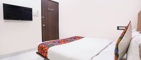 A bedroom with a bed, a wardrobe, a television, and a wall-mounted power outlet.