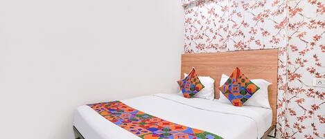 A bed with a colorful geometric-patterned bedspread, two pillows with similar patterns, and a wall with a floral wallpaper design.