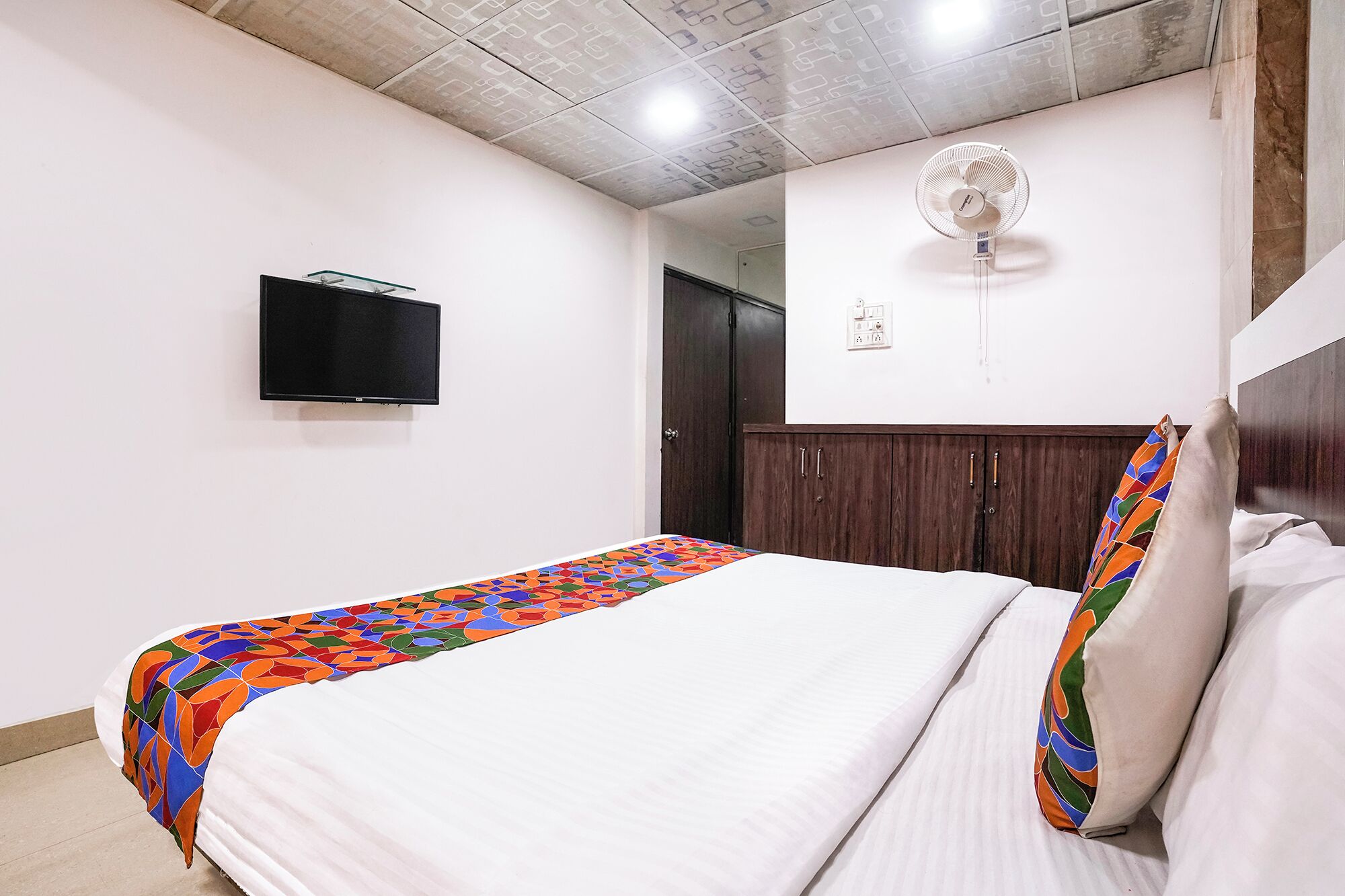 A bedroom with a bed, a TV, a wardrobe, and a ceiling fan.