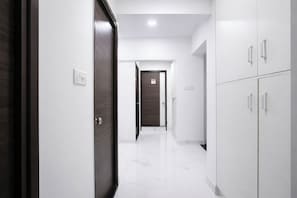 Un pasillo con una puerta de madera oscura, paredes blancas y suelo de baldosas blancas.