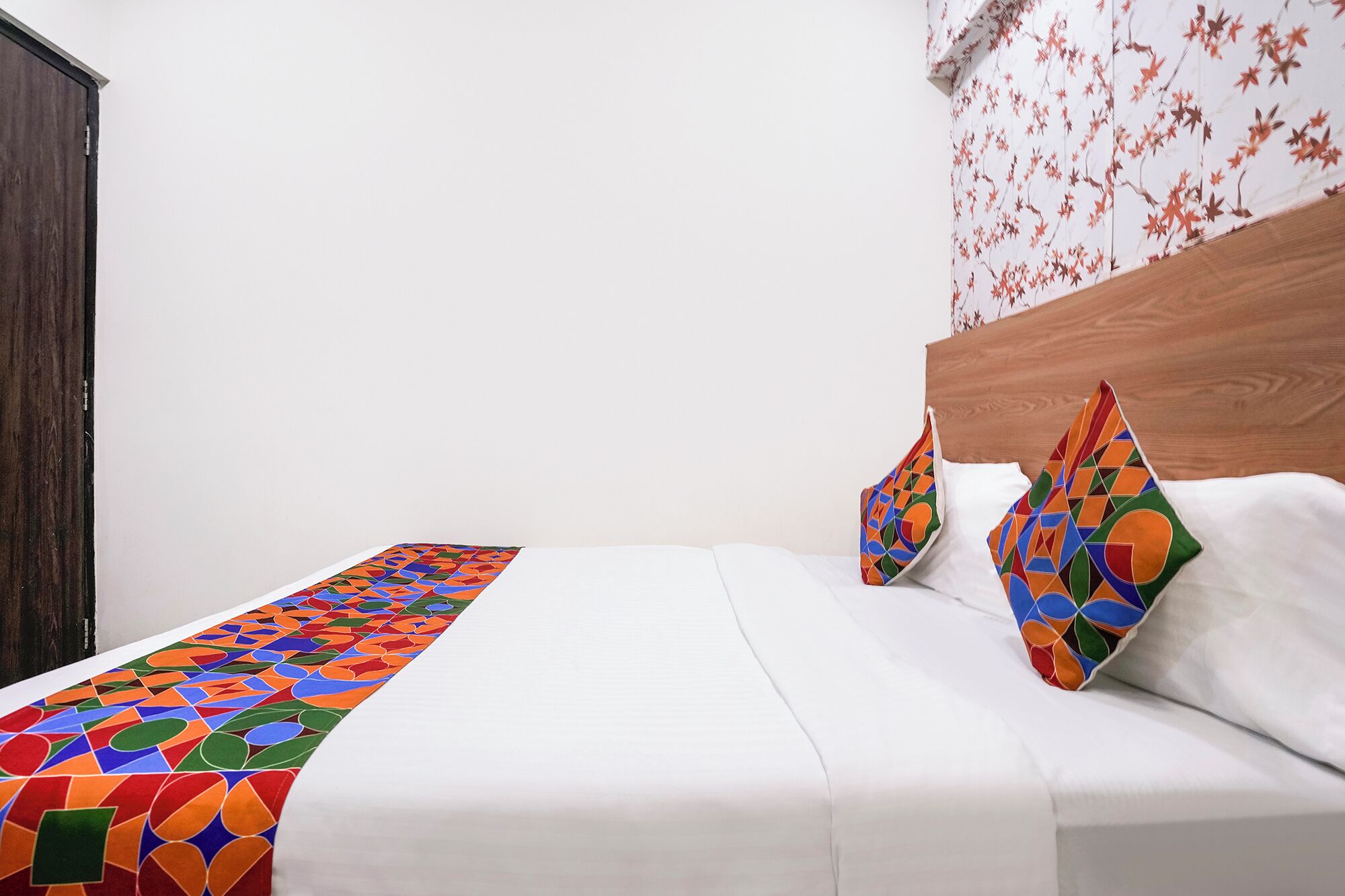 A bed with a colorful geometric-patterned runner, white bedding, and two pillows with a similar pattern.