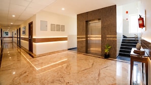 A hotel lobby with a marble floor, a reception desk, a staircase, and a fire extinguisher. - Fabhotel Grand & Resorts (Tirupporur)