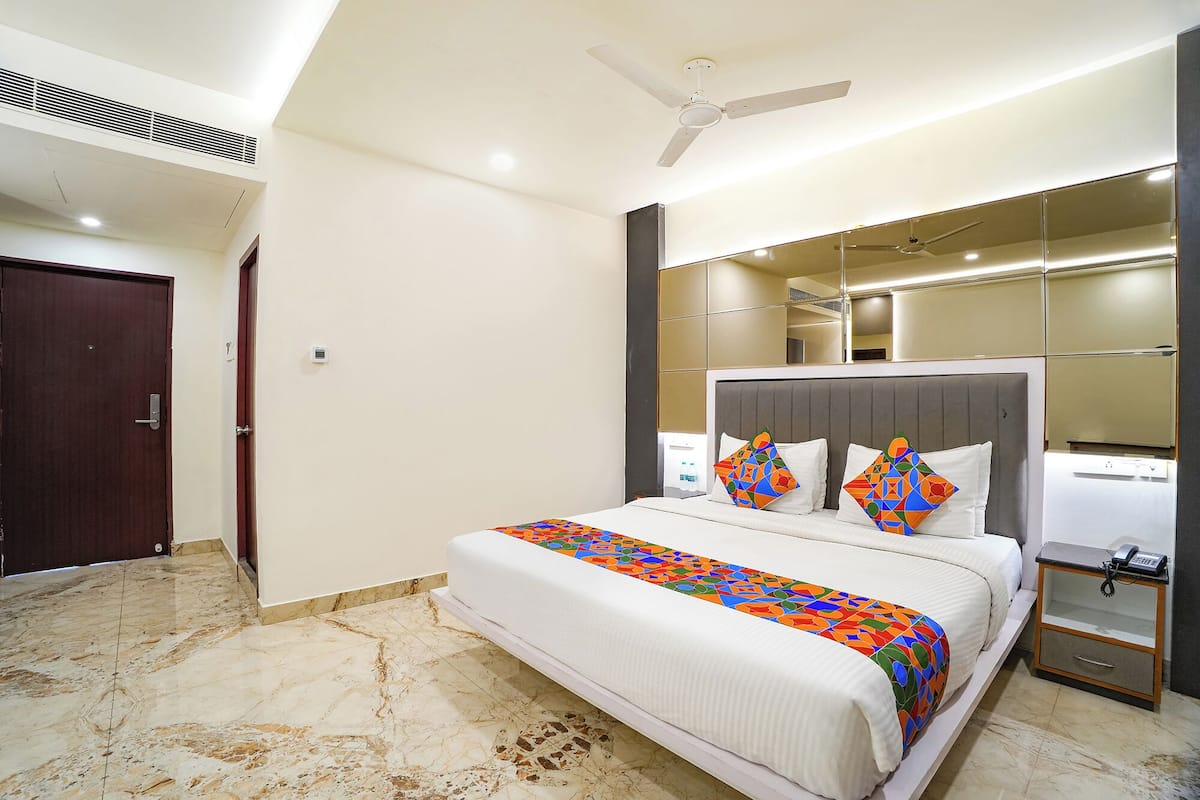 Een hotelkamer met een bed, nachtkastje, spiegel, plafondventilator en een deur.