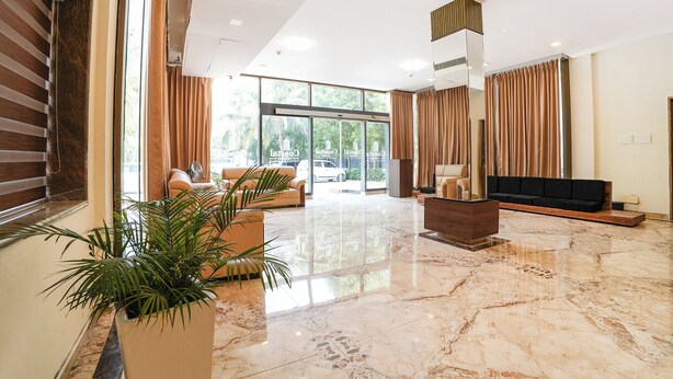 A spacious lobby with a marble floor, a sofa, a TV, and a large window with curtains. - Fabhotel Grand & Resorts (Tirupporur)