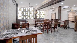 Un restaurante con mesas y sillas de madera, ventanas amplias, ventiladores de techo y paneles decorativos en las paredes.