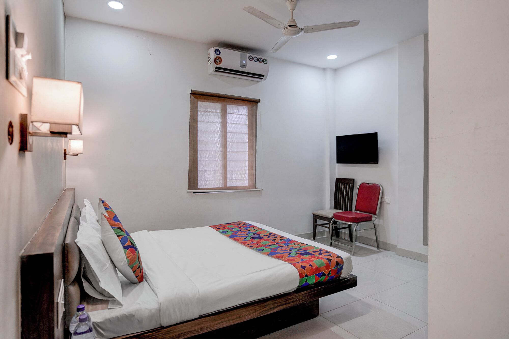 Une chambre à coucher comprenant un lit, un ventilateur de plafond, un climatiseur, une fenêtre, un téléviseur et une chaise.