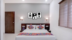 Una habitación de hotel con una cama, cabecera de madera, mesita de noche, luz de pared y una puerta.