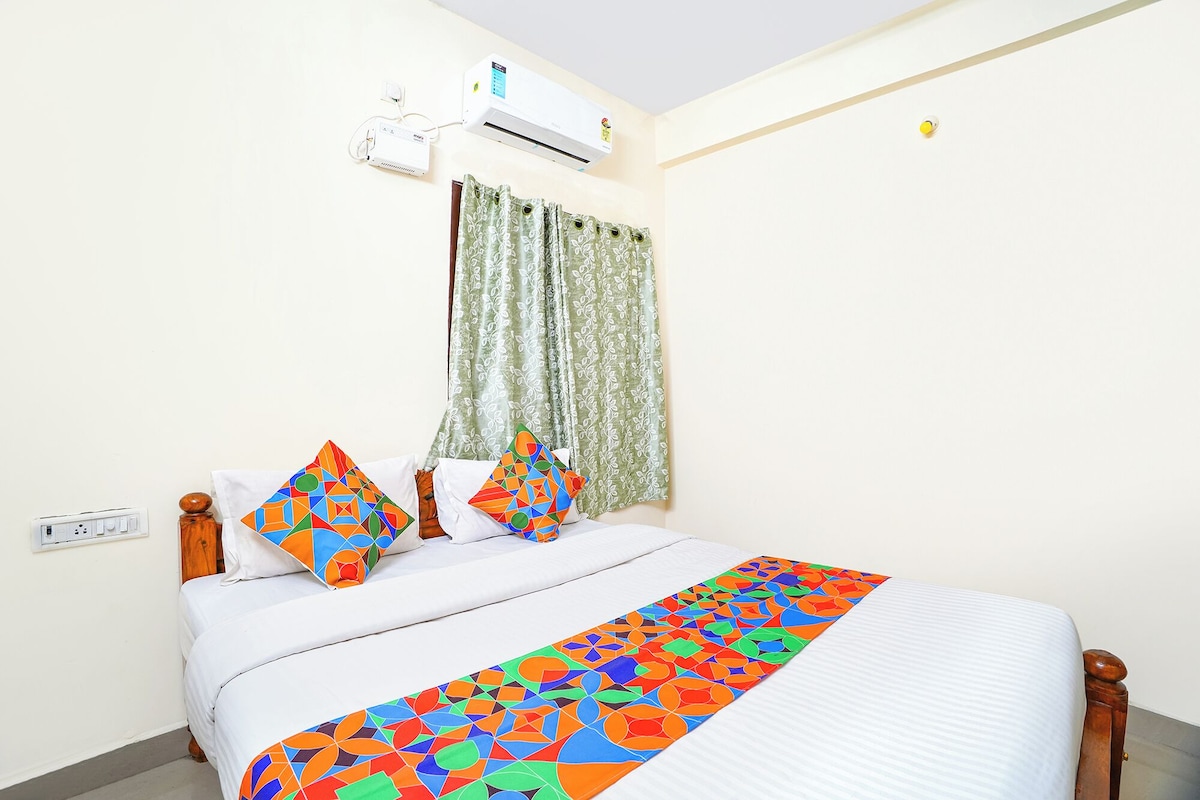 Una cama con una colcha de diseño geométrico y colores vivos, una pared blanca, una ventana con cortinas verdes y un equipo de aire acondicionado.