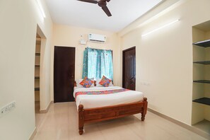 Un dormitorio con cama, ventilador de techo, equipo de aire acondicionado, ventana con cortinas y puerta.