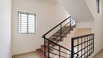 A staircase with a metal railing, a window with bars, and a plain wall.