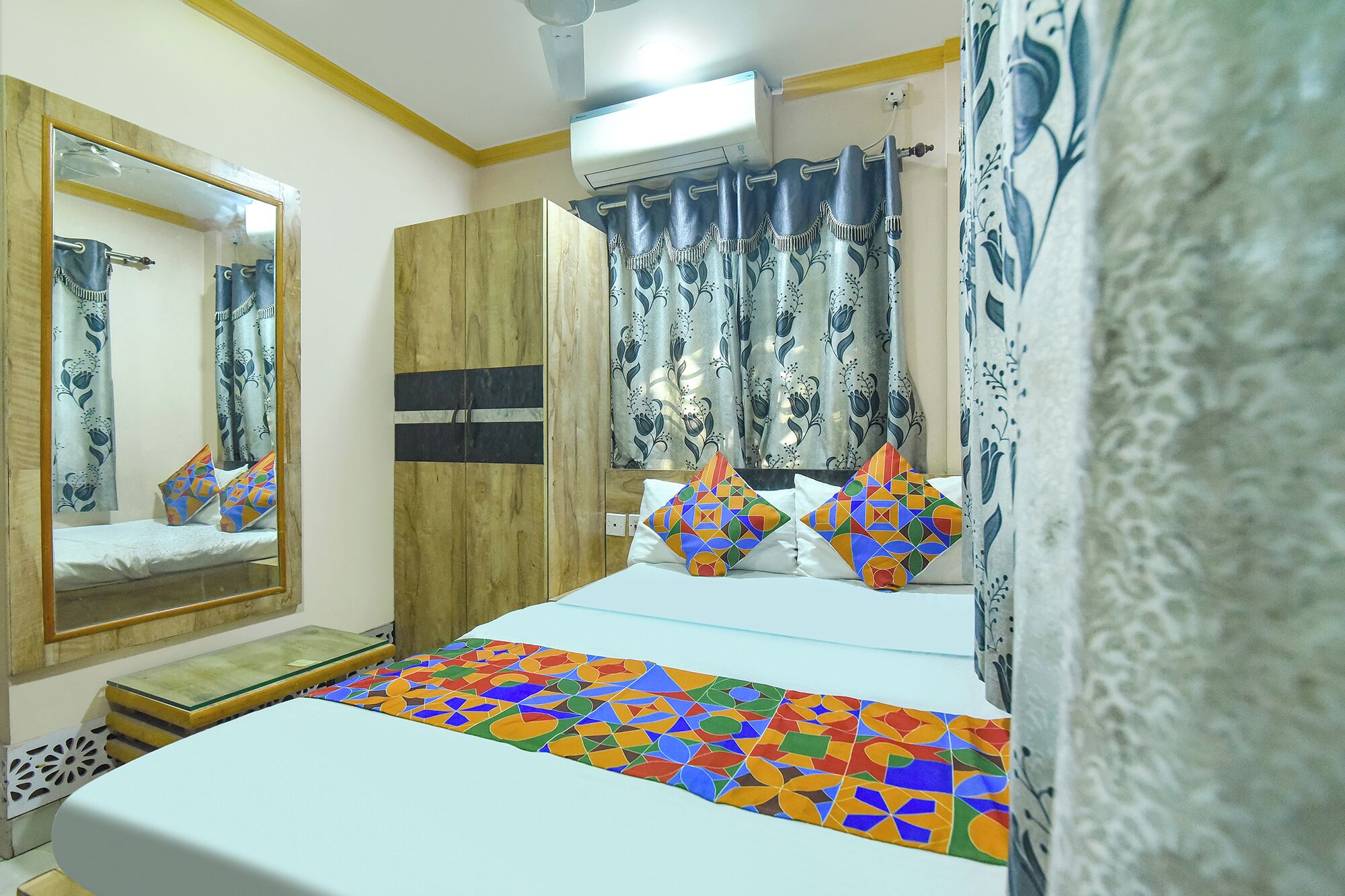 A bedroom with a bed, a mirror, a wardrobe, curtains, and a ceiling fan.