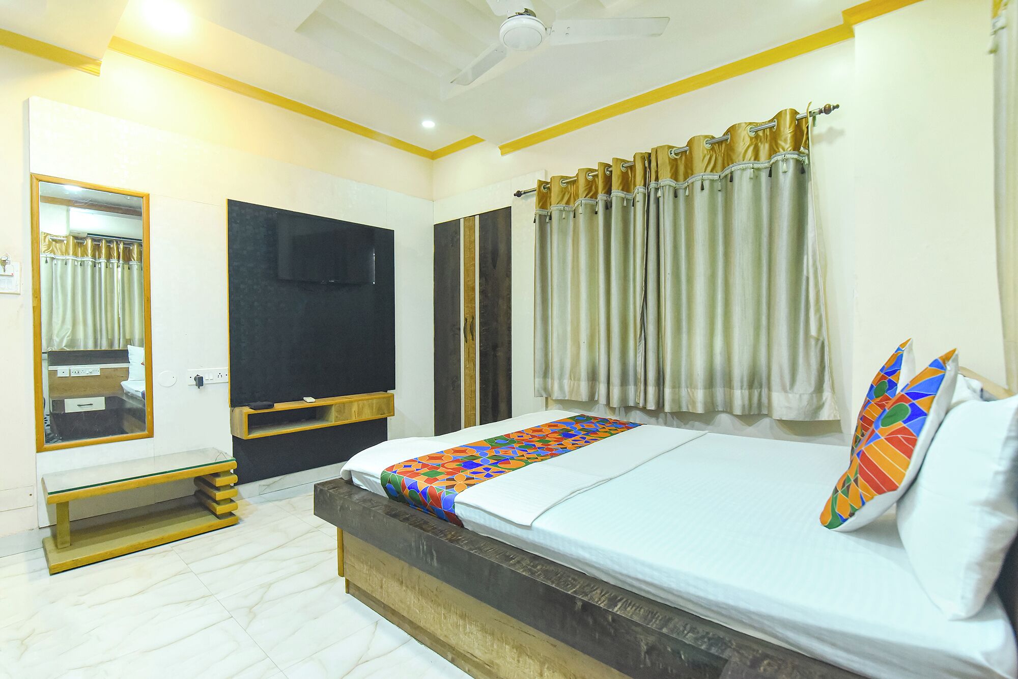 A bedroom with a bed, a mirror, a television, and a ceiling fan.