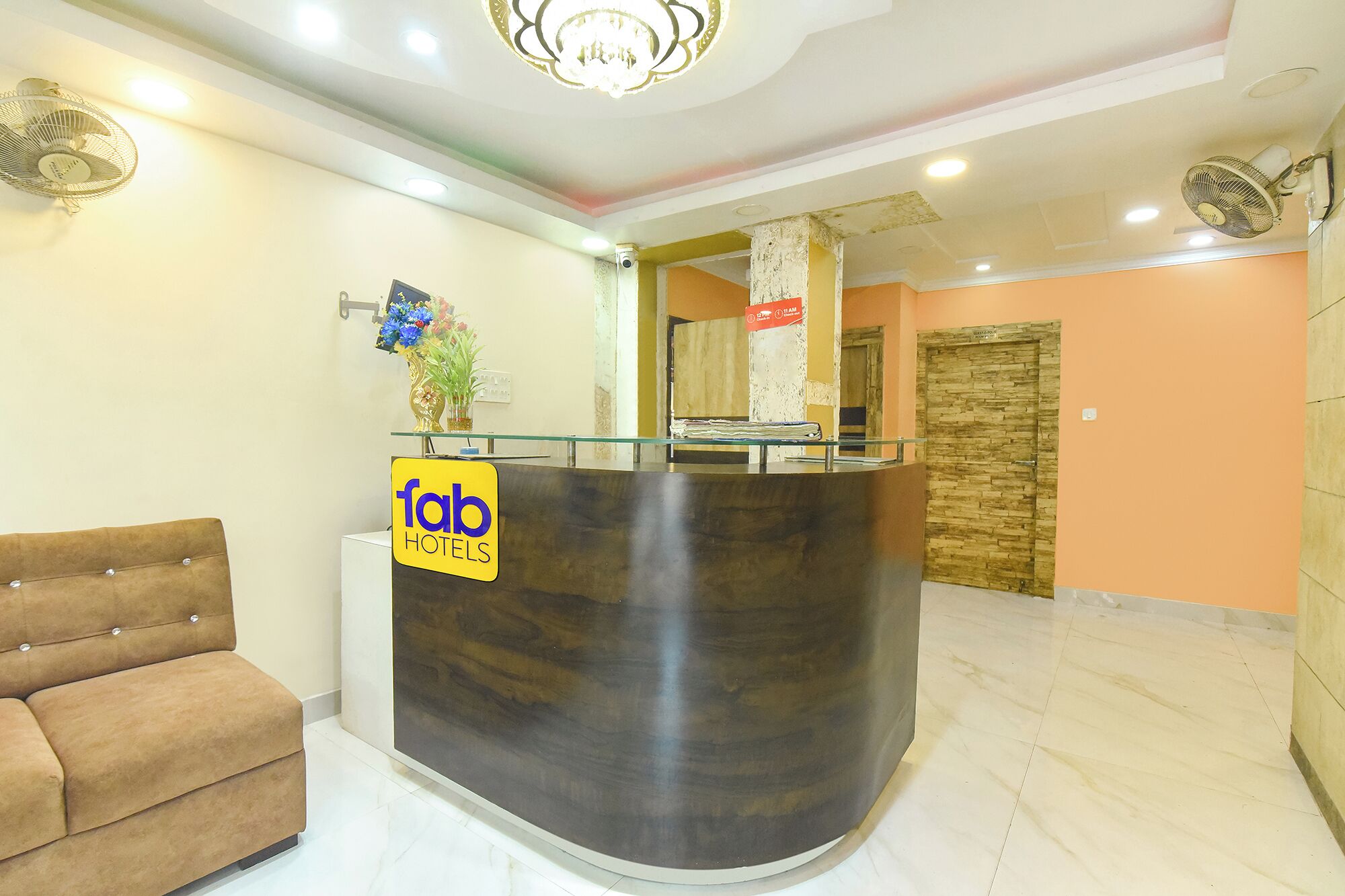 Una reception con una insegna che dice 'fab hotels', un divano marrone e un’area accoglienza con una parete in pietra e una porta in legno.