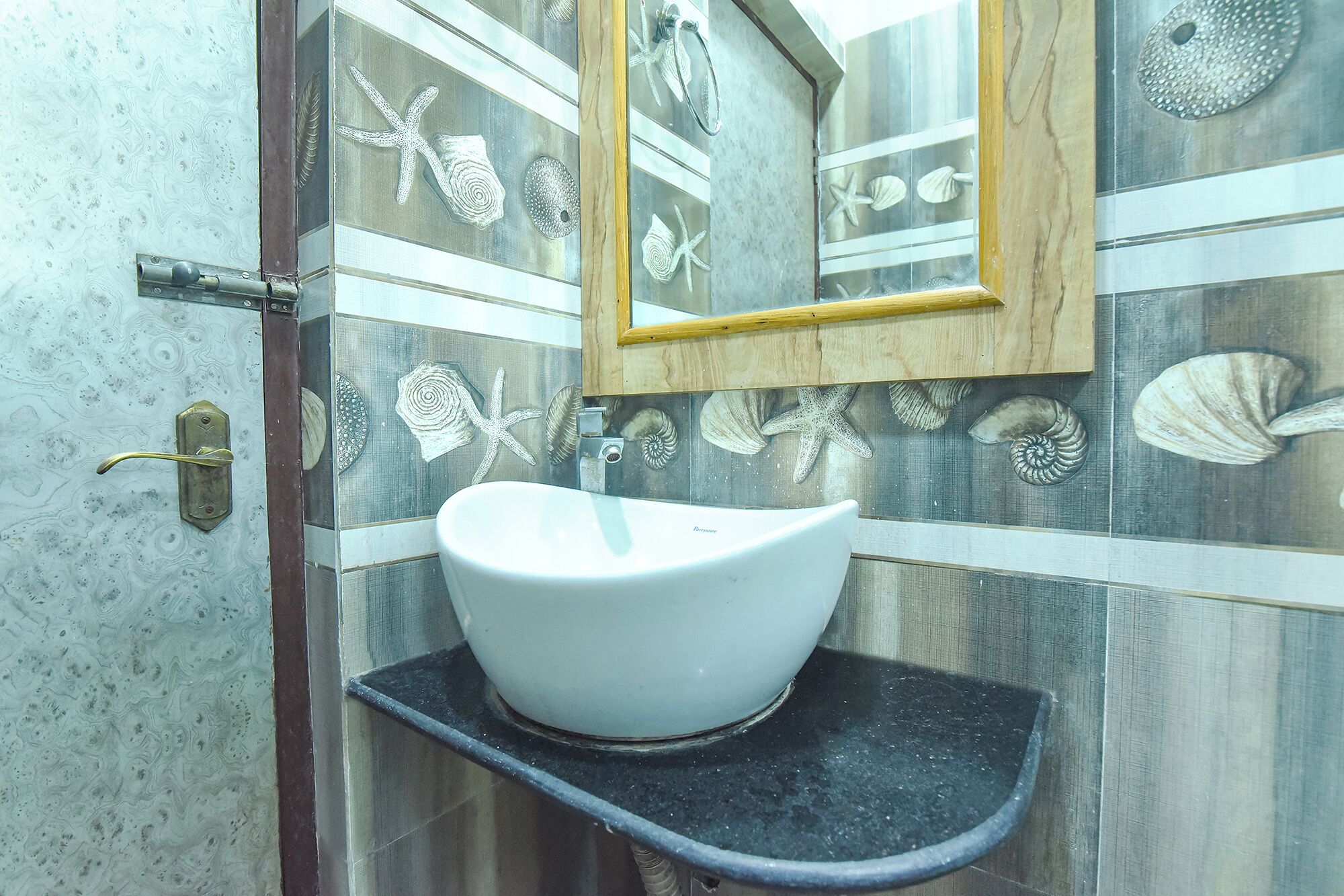 A bathroom with a white sink, a wooden-framed mirror, and decorative shell tiles.