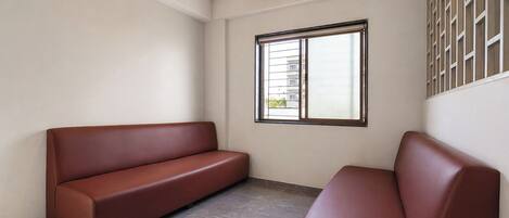 A room with a brown leather sofa, a window with metal bars, and a ceiling with wooden beams.