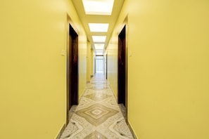 A long, narrow hallway with yellow walls and a patterned floor, leading to a bright room at the end. - Fabhotel Jagadish Palace (Puri)