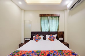 A hotel room with a bed, two nightstands, a window with curtains, and an air conditioning unit. - Fabhotel Jagadish Palace (Puri)