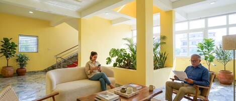 A spacious lobby with a yellow wall, a staircase, and potted plants.