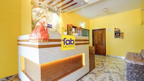 Egy szállodai recepció, amelyen egy „tab hotels” feliratú tábla található, egy szobor, valamint egy recepciós tér, ahol egy fa ajtó és márványburkolat látható.