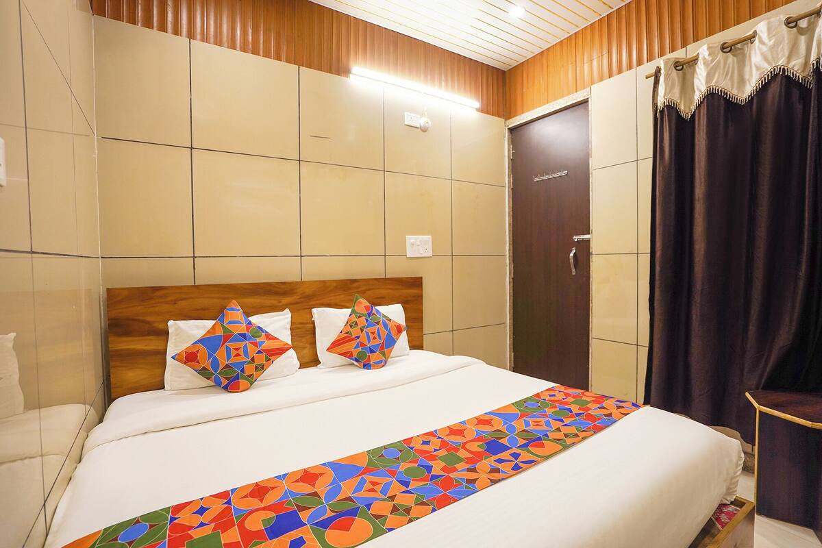 Una habitación de hotel con cama, cabecera, mesita de noche, puerta y cortina.