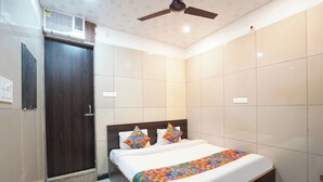 A modern hotel room with a large bed, a ceiling fan, and a door. - FabHotel BlueBell Inn (Lucknow)