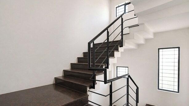 Eine moderne Treppe mit Metallgeländer, weißen Wänden und einem Fenster mit Gitterstruktur.