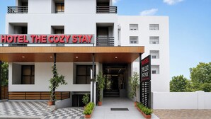 Ein Hotel namens 'Hotel The Cozy Stay' mit modernem Design, einem Schachbrettmuster-Eingang und Topfpflanzen.