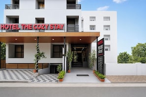 Um hotel chamado 'Hotel The Cozy Stay', com design moderno, entrada xadrez e plantas em vasos.