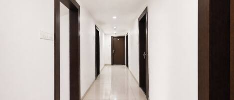 A corridor with white walls, dark wooden doors, and a tiled floor.