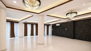 A spacious hotel room with a large open area, two chandeliers, a black textured wall, and a large window with curtains. - Fabhotel The Muffet (Indore)