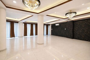 Une chambre d’hôtel spacieuse dotée d’un grand espace ouvert, de deux lustres, d’un mur noir à texture et d’une grande fenêtre avec des rideaux.