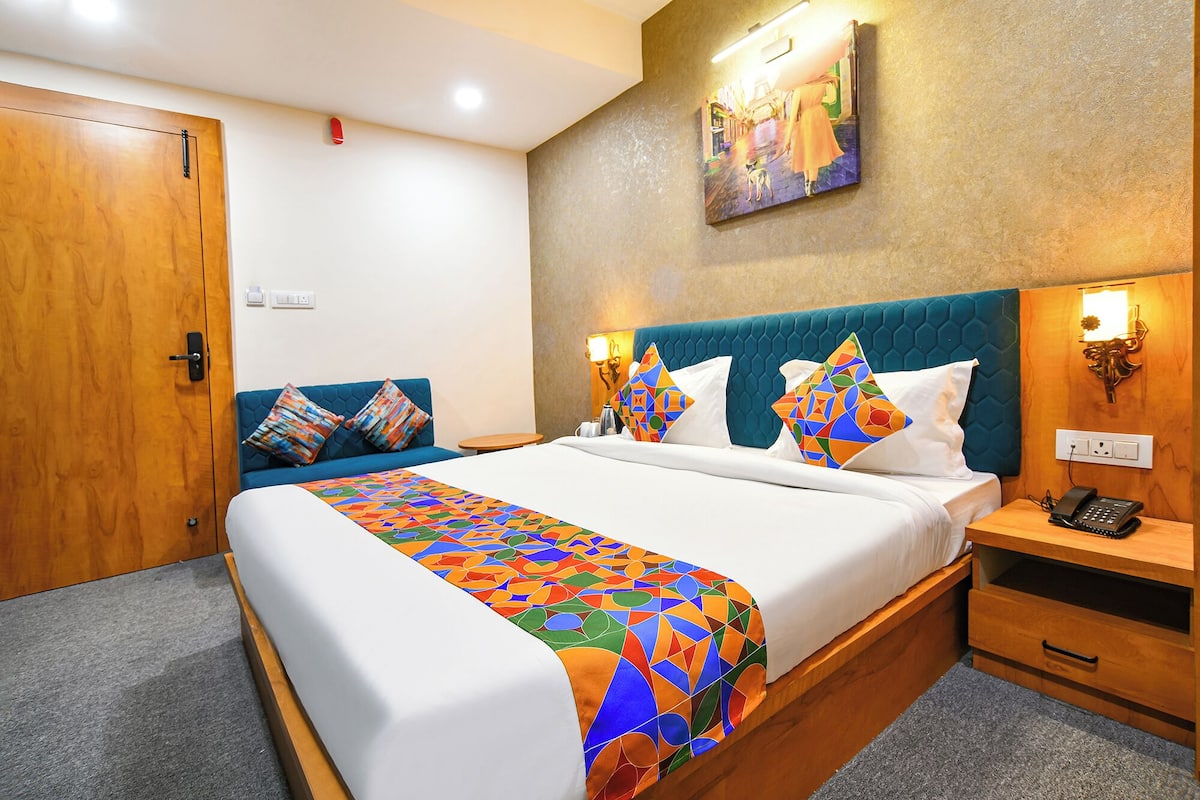 A hotel room with a bed, a blue sofa, a nightstand with a phone, and a painting on the wall.