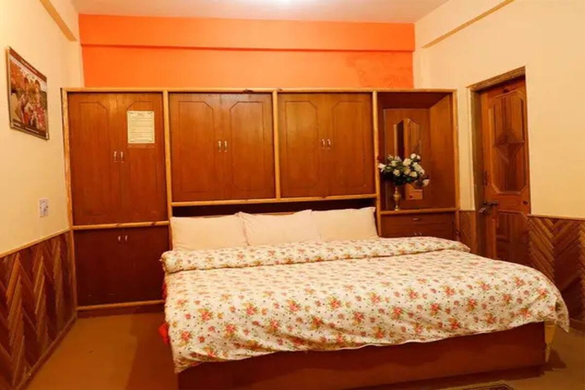 A bedroom with a bed, wooden wardrobe, and a small table with a vase.