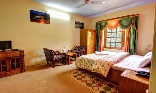 A bedroom with a bed, a desk, a chair, a television, and a window with curtains. - FabHotel Ballu’s Cafe & Resort (Manali)
