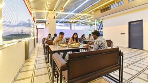 A dining area with tables and benches, a high ceiling with exposed beams, and a view through a mesh window. - Fabhotel The Nine Prime (Jaipur)