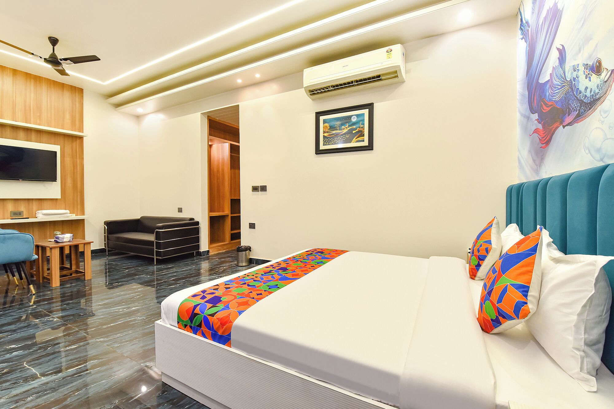 A hotel room with a bed, a desk, a chair, a TV, an air conditioner, and a door.