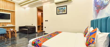 A hotel room with a bed, a desk, a chair, a TV, an air conditioner, and a door.