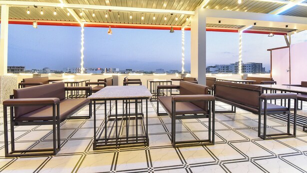 An outdoor seating area with tables and chairs, a view of the cityscape, and a metal roof structure. - Fabhotel The Nine Prime (Jaipur)