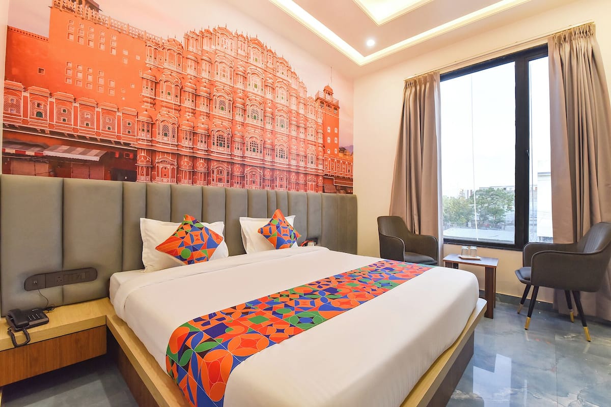 A hotel room with a large bed, a desk, a chair, a phone, and a window with curtains.