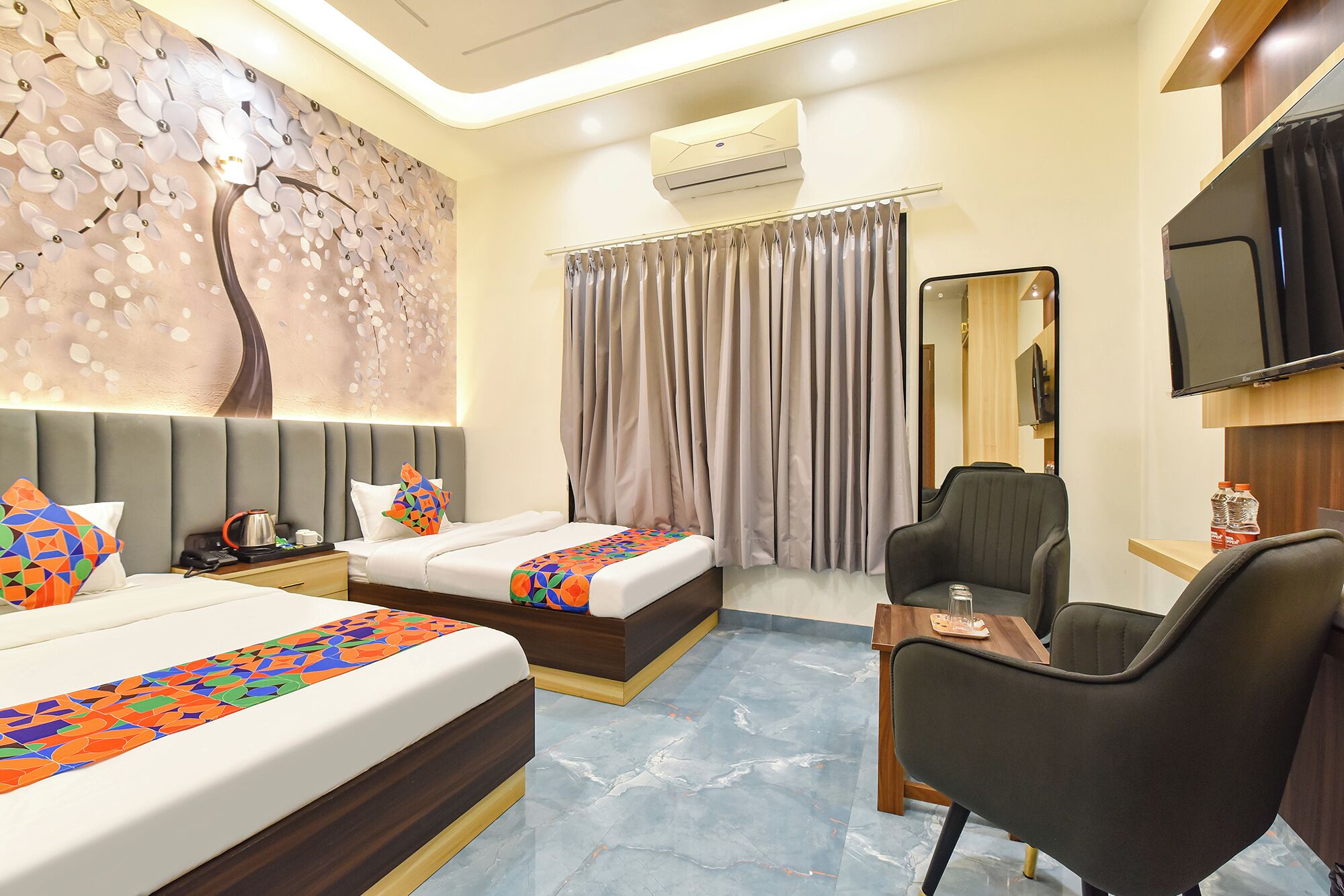 A hotel room with two beds, a desk, a chair, a TV, and an air conditioning unit.