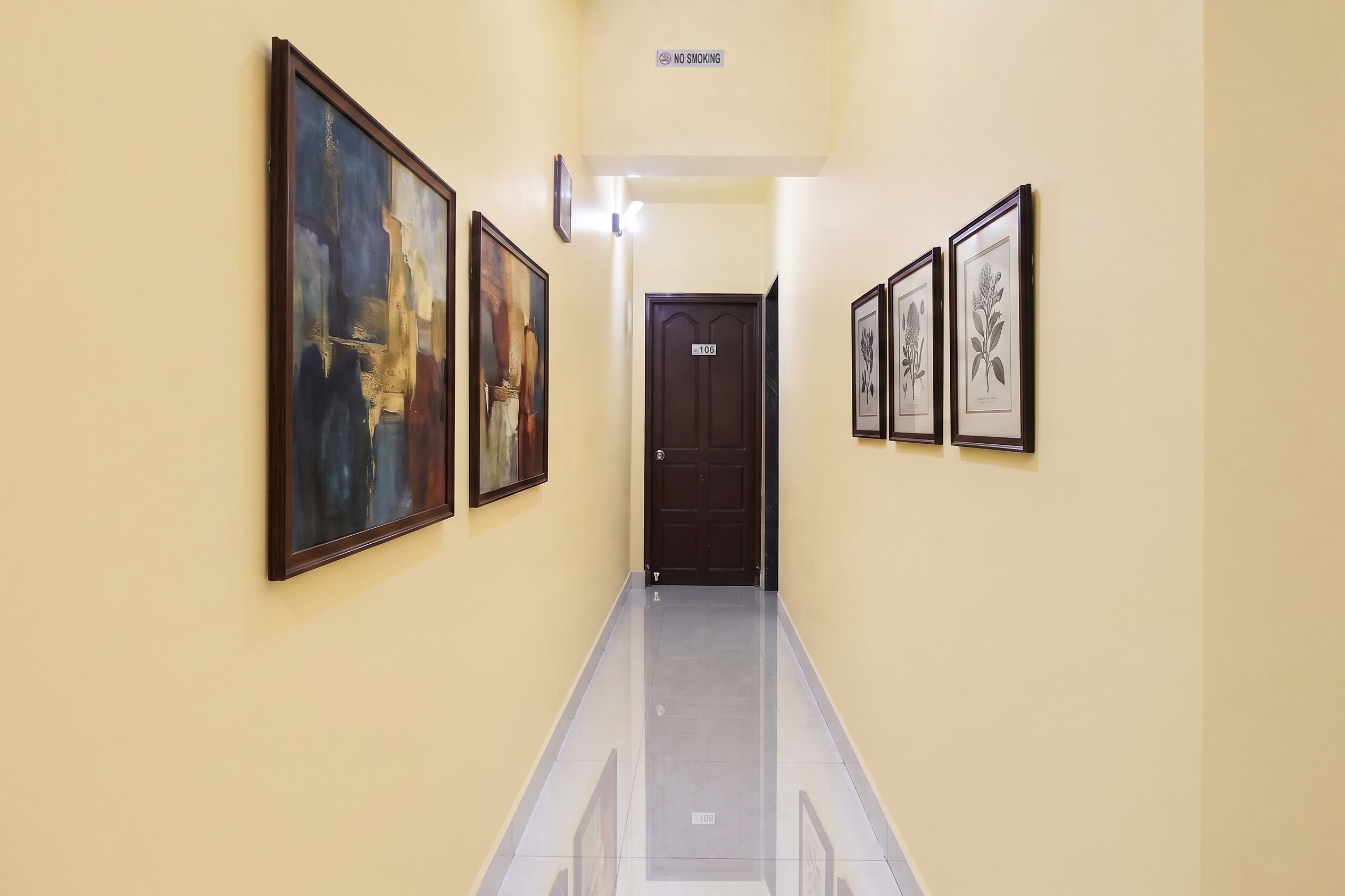 A hallway with framed artwork on the walls, a 'NO SMOKING' sign, and a door labeled '106'.