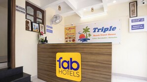 A reception desk with a sign for 'fab hotels' and another sign for 'Triple Beach Guest House' with a beach and palm tree graphic. - FabHotel Triple Beach House - Nr. Benaulim Beach (Morjim)